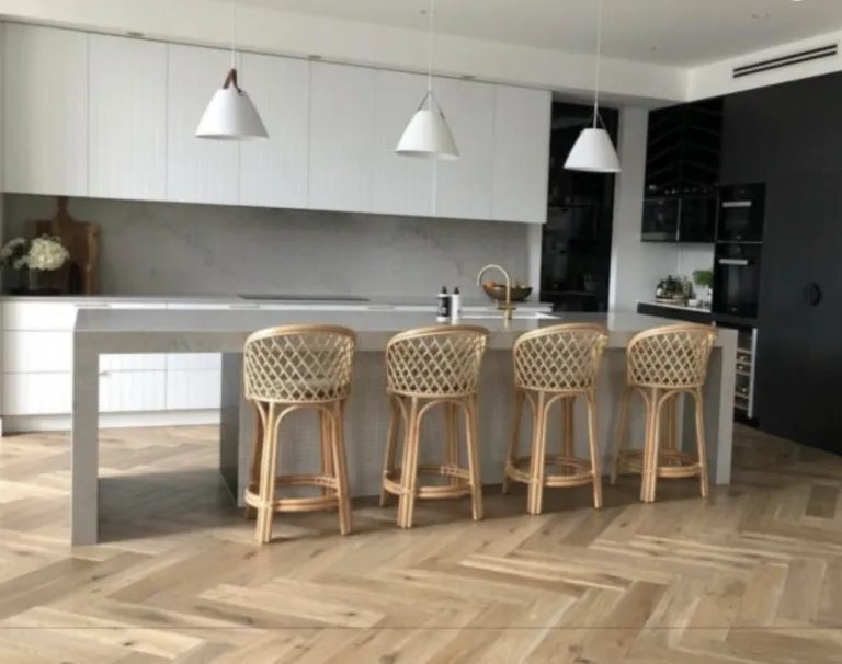 Natural oak herringbone in a white kitchen with rattan stools and pendant lights