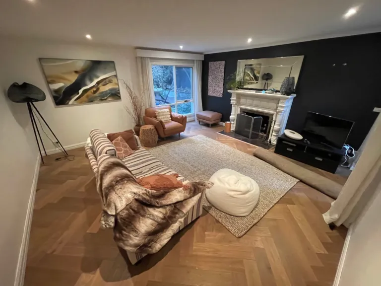 Sherbrooke Oak herringbone parquetry in a lounge with a white fireplace and dark feature wall