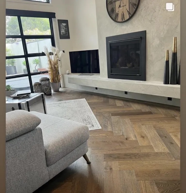 Sherbrooke Oak herringbone in a living room with a concrete fireplace and grey sofa
